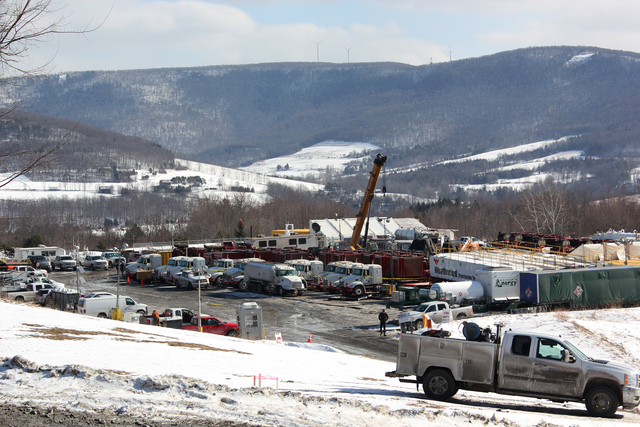 Landscape shot with snowy hills in the background. In the foreground a parking lot filled with flatbed trucks carrying machinery and a construction crane.