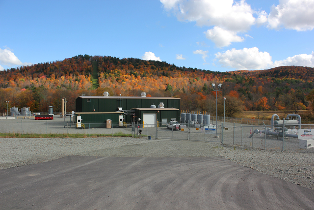 A small commercial building clad in green metal siding, surrounded by a chain-link fence.