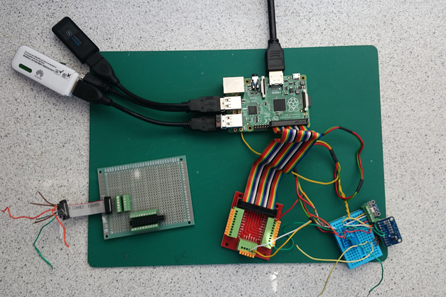 A small collection of circuit boards on a green mat, some connected to one another by wires and USB cables.