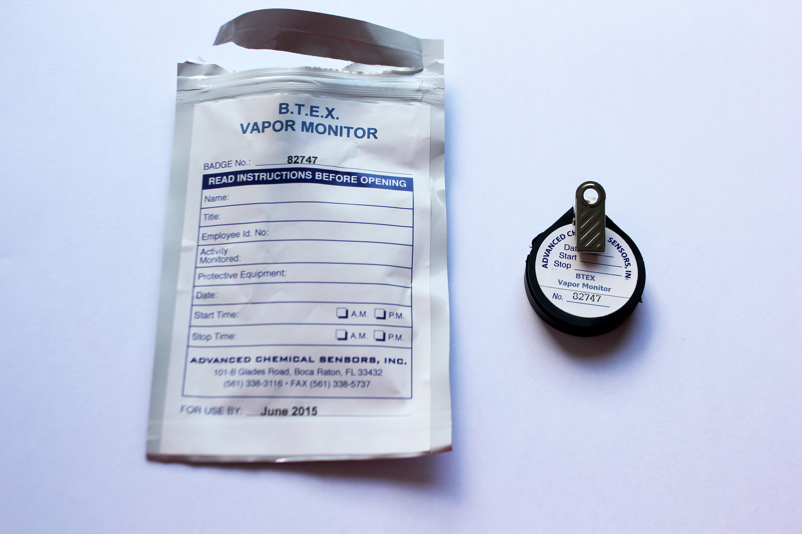 An open vapor-sealed bag with sticker prompting for name and date and timing information beside a circular monitor in black casing with a badge clip.